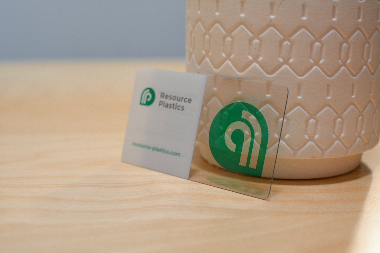 A single plastic business card printed on clear plastic with a vase visible behind